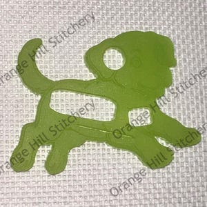 May include: A green plastic cutout of a dog, possibly a pug, with a hole in the ear. The cutout is on a white background.