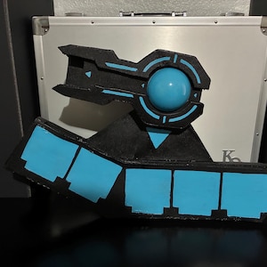 Op de afbeelding: Een rekwisiet van zwart schuim met een centrale blauwe bol en geometrische blauwe accenten. Het ontwerp bevat een horizontale basis met vijf rechthoekige blauwe panelen en een bovengedeelte met een cirkelvormig frame van zwart schuim.
