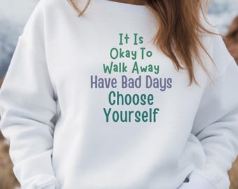 May include: White sweatshirt with the text "It Is Okay To Walk Away Have Bad Days Choose Yourself" in green and purple. The sweatshirt is a crew neck style and appears to be made of a soft material.