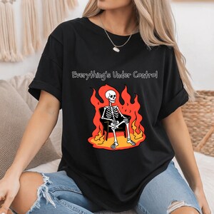 May include: Black t-shirt with a graphic of a skeleton sitting in a chair engulfed in flames. The text "Everything's Under Control" is printed above the graphic.