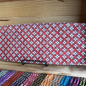 May include: Rectangular red ceramic serving platter with a white floral pattern. The platter is supported by a black metal stand and is displayed on a wooden shelf. The floral design is repeated across the entire surface.