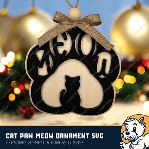 K&ouml;nnte beinhalten: Ein Holzornament in Form einer Katzenpfote mit dem ausgeschnittenen Wort "MEOW" und einer Katzen-Silhouette. Es hat eine Schleife aus Jute und eine Holzperle zum Aufh&auml;ngen. Der Text "CAT PAW MEOW ORNAMENT SVG" steht unten.