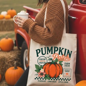 May include: A cream-colored canvas tote bag featuring a graphic print with the text PUMPKIN PATCH, FRESH FROM THE PATCH, FARM FRESH, LOCALLY GROWN, AUTUMN PICKED, PUMPKINS, CORN MAZE, and APPLE CIDER, centered around a large orange pumpkin illustration.