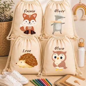 Könnte beinhalten: Vier beige Rucksäcke mit Kordelzug, personalisierten Namen und Aquarell-Tierillustrationen. Die Taschen zeigen einen Fuchs mit dem Namen Emma, einen Dachs mit dem Namen Oliver, einen Igel mit dem Namen Leon und eine Eule mit dem Namen Olivia.