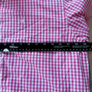 May include: A pink and white gingham-patterned shirt with a button-down collar and a chest pocket. The shirt has a small embroidered logo on the pocket. The ruler shows the shirt is approximately 20 inches wide.