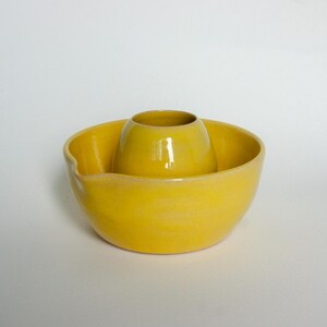 May include: A bright yellow ceramic juicer with a built-in reamer. The juicer has a rounded bowl shape with a pouring spout and a central cone for citrus fruits. The glossy finish enhances its vibrant color.