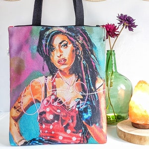 Puede incluir: Una bolsa de lona negra con una imagen colorida de una mujer con una corona y la palabra "Queen" en letras rosas. La mujer lleva un vestido de lunares rojos y blancos y guantes azules.