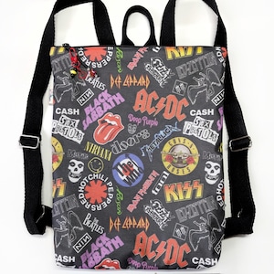 May include: Black backpack featuring a black and white print of various rock band logos, including AC/DC, Black Sabbath, KISS, The Beatles, and Nirvana. The backpack has adjustable straps and a zip closure.
