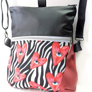 May include: Black and red crossbody bag with a zipped pocket and a zebra print lining featuring red hearts with eyes.