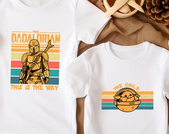 May include: Two white t-shirts with Star Wars-themed graphics. One shirt features "The Dadalorian" with a character illustration and the text "This is the Way." The other shirt displays "The Child" with a character illustration.