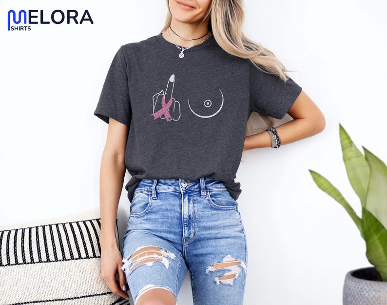 May include: Dark gray t-shirt with a graphic of a hand giving the middle finger, a pink ribbon, and a breast. The shirt is made of a soft material and is a crew neck style.