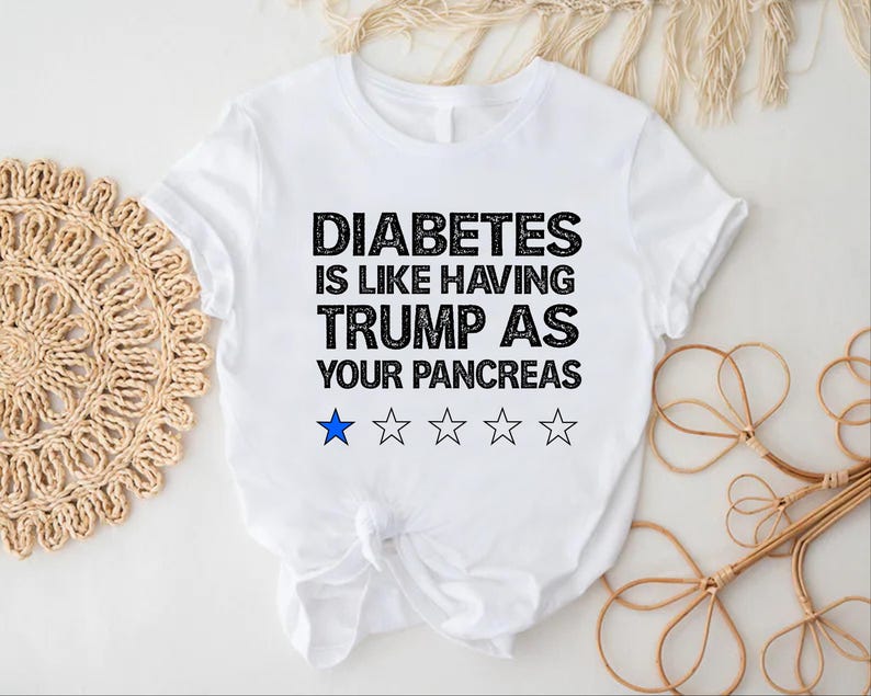 Puede incluir: Camiseta blanca con texto negro que dice "La diabetes es como tener a Trump como p&aacute;ncreas". Hay cinco estrellas negras y una estrella azul debajo del texto.
