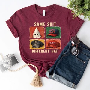 May include: Maroon t-shirt with the text "SAME SHIT DIFFERENT HAT" and four images of different hats. The shirt is paired with blue denim shorts and sunglasses. A camera and decorative beads are also in the image.