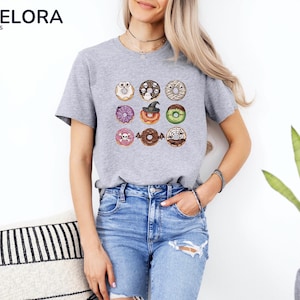 Puede incluir: Camiseta gris jaspeado con un dise&ntilde;o de nueve donuts con tem&aacute;tica de Halloween. Los donuts est&aacute;n decorados con calaveras, telara&ntilde;as y un sombrero de bruja. La camiseta tiene mangas cortas y cuello redondo.