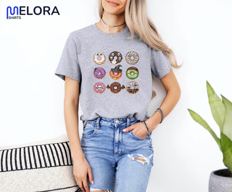Puede incluir: Camiseta gris jaspeado con un dise&ntilde;o de nueve donuts con tem&aacute;tica de Halloween. Los donuts est&aacute;n decorados con calaveras, telara&ntilde;as y un sombrero de bruja. La camiseta tiene mangas cortas y cuello redondo.