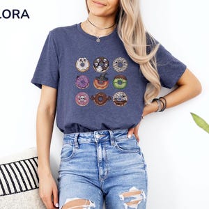 Puede incluir: Camiseta azul marino con una cuadr&iacute;cula de nueve donuts tem&aacute;ticos de Halloween. Cada donut tiene decoraciones &uacute;nicas, incluyendo fantasmas, telara&ntilde;as y calaveras. La camiseta es de material suave y es adecuada para uso casual.