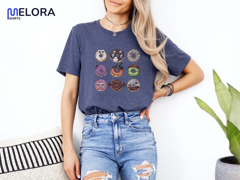 Puede incluir: Camiseta azul marino con una cuadr&iacute;cula de nueve donuts tem&aacute;ticos de Halloween. Cada donut tiene decoraciones &uacute;nicas, incluyendo fantasmas, telara&ntilde;as y calaveras. La camiseta es de material suave y es adecuada para uso casual.