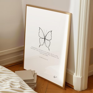 Può includere: Una stampa artistica incorniciata con una cornice dorata, raffigurante un'illustrazione di farfalla in bianco e nero. La stampa include il testo "Therefore if anyone is in Christ, he is a new creation... II Corinthians 5:17."