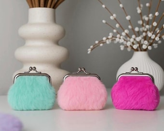 Puede incluir: Tres monederos esponjosos en tonos turquesa, rosa y magenta. Cada monedero tiene un cierre plateado y un exterior suave y texturizado. Perfectos para guardar monedas o pequeños objetos.