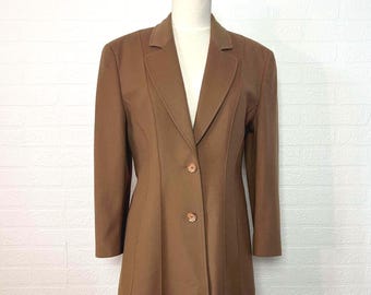 Könnte beinhalten: Ein brauner Blazer mit fallendem Revers und Zwei-Knopf-Verschluss. Die maßgeschneiderte Jacke hat lange Ärmel und vertikale Nähte für eine strukturierte Silhouette. Der Blazer wird auf einer Schaufensterpuppe mit Holzständer präsentiert.