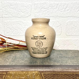 Peut inclure: Un pot en céramique beige avec une finition mouchetée et un col étroit. L'avant présente un texte noir indiquant "green label" CURRY PASTE, 5 1/2 oz NET, Ingredients: Curry Powder, Malt Vinegar, Edible Oil, MADE IN ENGLAND BY J.A. SHARWOOD & CO. LTD.