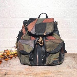 Peut inclure: Un sac à dos patchwork aux tons noir, marron, vert et rouille. Le sac est doté d'une fermeture à rabat avec un fermoir en laiton et de deux poches avant. Le design intègre diverses formes et textures géométriques, créant une esthétique vintage unique.
