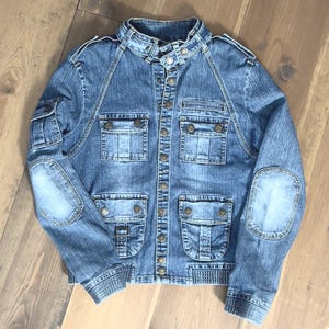 Distressed blue faded motorcycle-style denim jacket with multiple pockets and star-shaped snap buttons / Size S/M