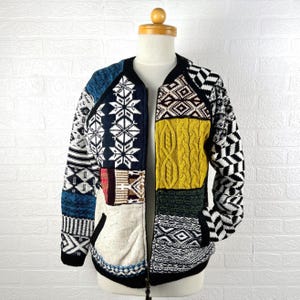 Könnte beinhalten: Eine Patchwork-Jacke mit Reißverschluss und einer Vielzahl von Mustern und Farben. Die Jacke hat geometrische, Zopfstrick- und Schneeflocken-Designs in Blau-, Gelb-, Schwarz-, Weiß- und Rottönen. Die Jacke wird auf einer Schaufensterpuppe präsentiert.