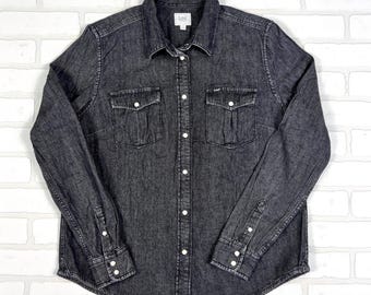 May include: A dark gray denim shirt with a button-down front, two chest pockets, and buttoned cuffs. The shirt has a classic collar and the Lee logo is visible on the chest pocket and collar.