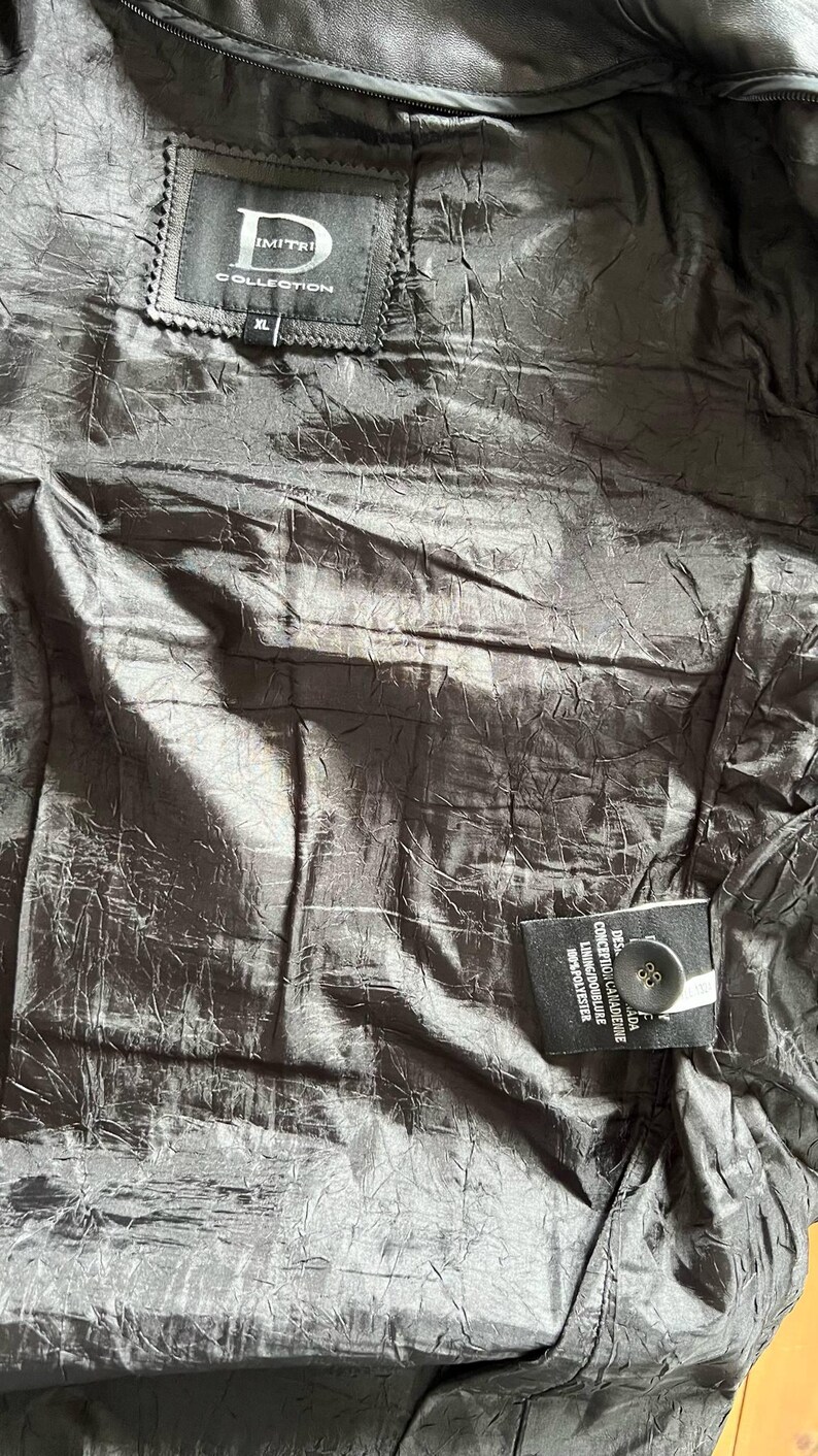 May include: Black leather jacket with a black label that says "Dimitri Collection" and "XL". The jacket has a black button and a label with the text "DESIGNED IN CANADA CONCEPUTA IN CANADA LINING/DOUBLURE 100% POLYESTER"