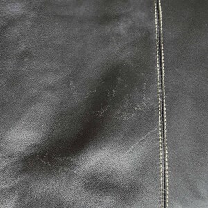 May include: Close-up of a black leather skirt with white stitching. The skirt has a slight sheen and a textured surface.