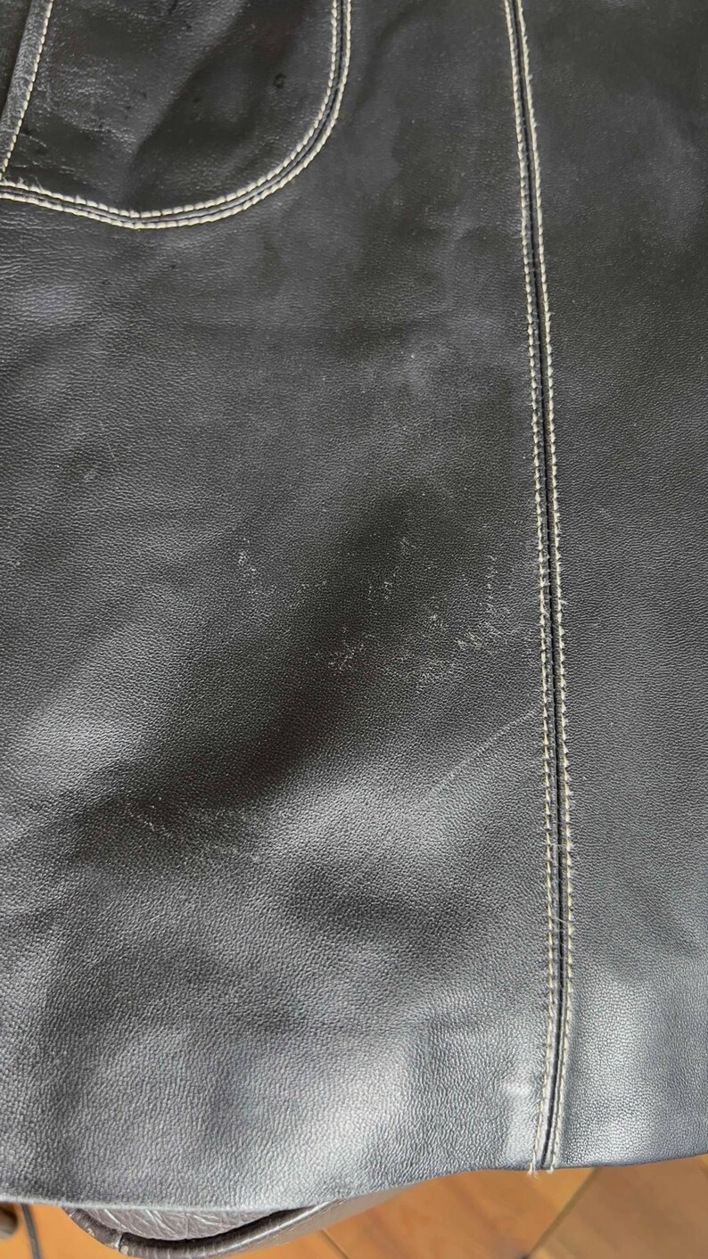 May include: Close-up of a black leather skirt with white stitching. The skirt has a slight sheen and a textured surface.
