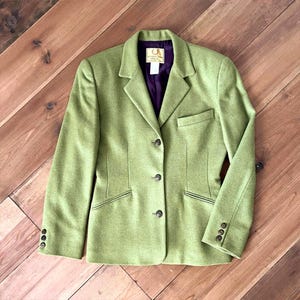 May include: A lime green blazer featuring a dark purple interior lining, a notched lapel, three front buttons, and three smaller buttons on each sleeve cuff. A single chest pocket and two side pockets are visible, along with a white brand label.