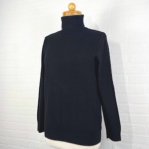 May include: A black ribbed knit turtleneck sweater displayed on a mannequin. The sweater has long sleeves and a high, folded collar. The fabric has a vertical ribbed texture.