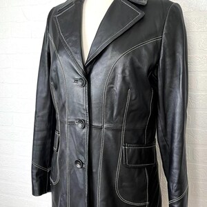 May include: A black leather jacket with white stitching. The jacket has a long, fitted silhouette and a button-up front.