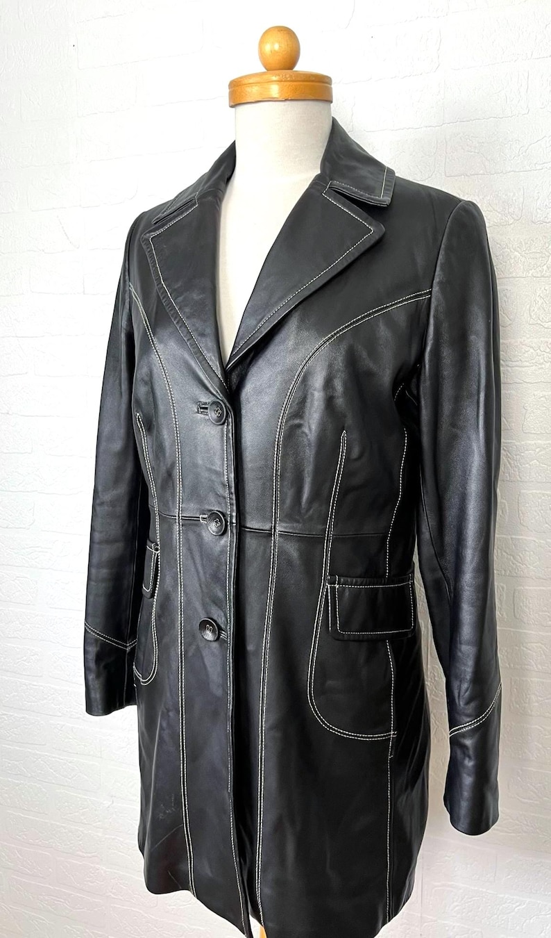 May include: A black leather jacket with white stitching. The jacket has a long, fitted silhouette and a button-up front.