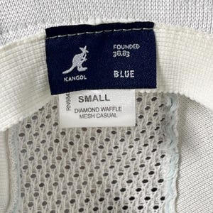 May include: A white Kangol hat interior featuring a dark blue rectangular tag with a white kangaroo logo and the text FOUNDED 38.83 BLUE. A white label below displays the text SMALL and DIAMOND WAFFLE MESH CASUAL, with a visible RN6848 number.