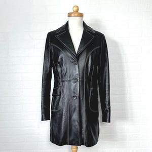 May include: A black leather coat with white stitching. The coat has a long, fitted silhouette and a button-up front.