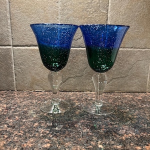 May include: Two blue and green glass wine glasses with a textured surface.