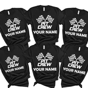 Op de afbeelding: Zes zwarte T-shirts met een wit geruit vlagontwerp en de tekst "Pit Crew Your Name" gedrukt op de voorkant.