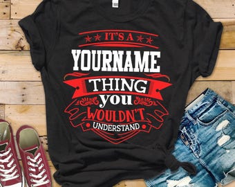 May include: A black short-sleeved t-shirt featuring a graphic design with red and white text that reads IT'S A YOURNAME THING YOU WOULDN'T UNDERSTAND, accented with decorative red banners and star motifs centered on the chest.