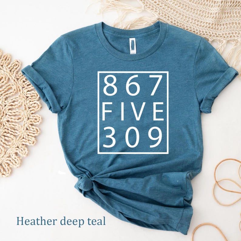 May include: A heather deep teal short-sleeve t-shirt featuring a white square graphic on the chest. Inside the square, the text reads 867 FIVE 309 in a clean, sans-serif font. The shirt has a crew neckline and is displayed with a knotted hem.