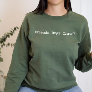 May include: An olive green sweatshirt with the words "Friends. Dogs. Travel." printed in white. The long-sleeved crew neck top is made of a soft material.