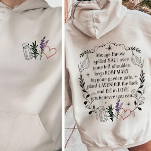 May include: A white hoodie with a black graphic print of a salt shaker, rosemary, lavender, and a heart. The text reads "Always throw spilled SALT over your left shoulder, keep ROSEMARY by your garden gate, plant LAVENDER for luck and fall in LOVE whenever you can."