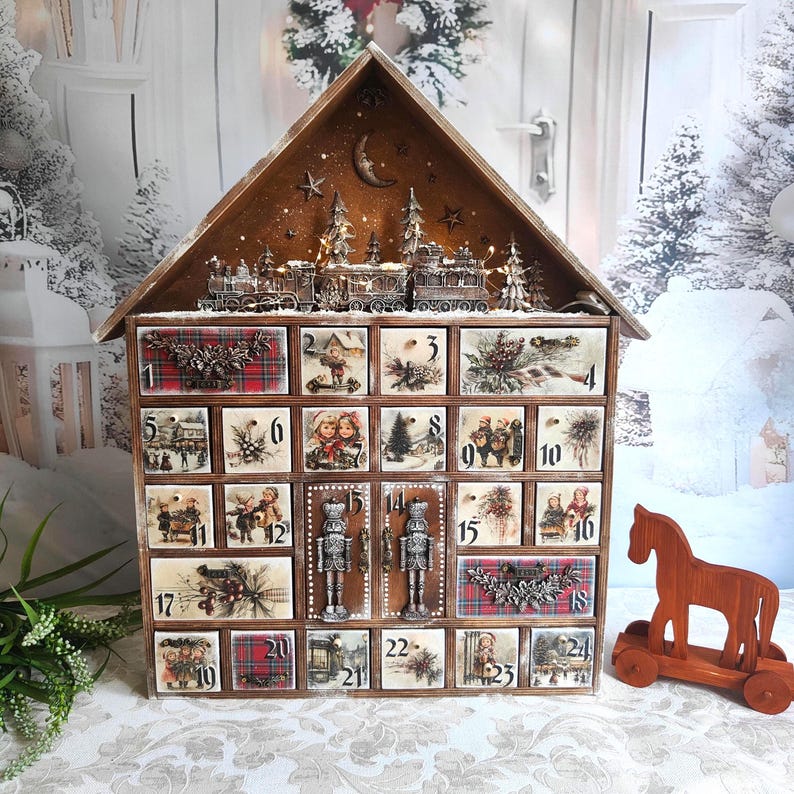 May include: A wooden house-shaped advent calendar with twenty-four numbered drawers. The drawers feature vintage-style illustrations of children, winter scenes, and red plaid patterns. A miniature train and nutcracker figures decorate the front.
