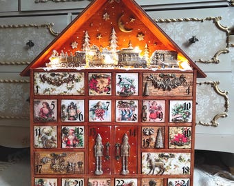 May include: A wooden advent calendar shaped like a house with twenty-four numbered drawers. The top features a miniature train scene with warm lights, stars, and a crescent moon. Each drawer displays unique vintage-style holiday illustrations.