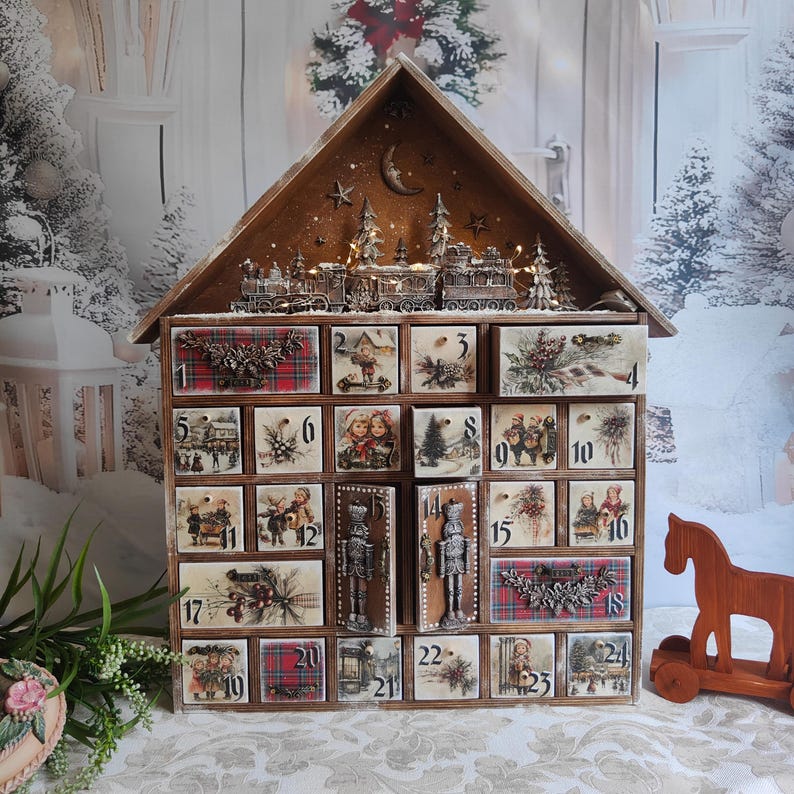 May include: A wooden house-shaped advent calendar with twenty-four numbered drawers. The drawers feature vintage-style illustrations of children, winter scenes, and red plaid patterns. A miniature train and moon motif sit on the roof.