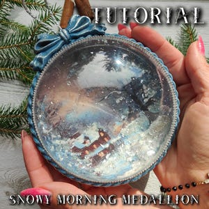 May include: A round, clear, flat-backed ornament featuring a winter scene with a brown house covered in snow. The frame is blue with a decorative bow at the top and a silver beaded edge. The text TUTORIAL and SNOWY MORNING MEDALLION are visible.
