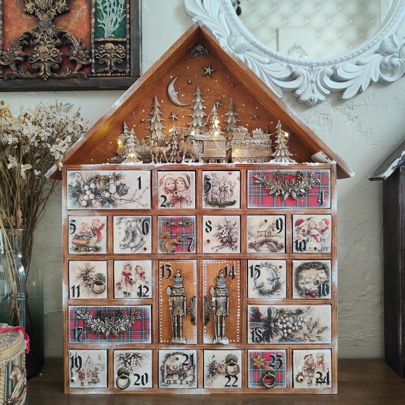 May include: A wooden house-shaped advent calendar with twenty-four numbered drawers. The top features a carved winter forest scene with a moon, stars, and deer. Each drawer displays vintage-style holiday illustrations, red plaid patterns, and metal pulls.