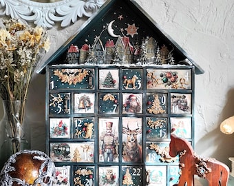 May include: A dark green wooden advent calendar shaped like a house with twenty-four numbered drawers. The top features a miniature village scene under a crescent moon. Each drawer displays unique Christmas-themed illustrations and gold-toned accents.